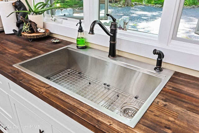 interior details with butcher block countertops, sink, and white cabinetry