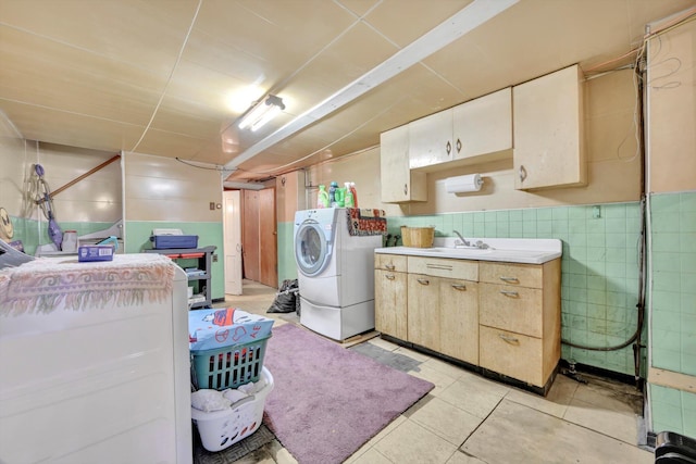 clothes washing area featuring a wainscoted wall, washer and dryer, a sink, cabinet space, and tile walls