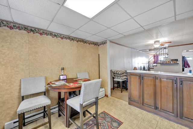 dining area featuring a drop ceiling, baseboard heating, and stairs