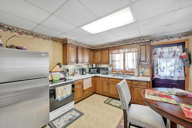 kitchen with light floors, light countertops, freestanding refrigerator, white electric stove, and a paneled ceiling