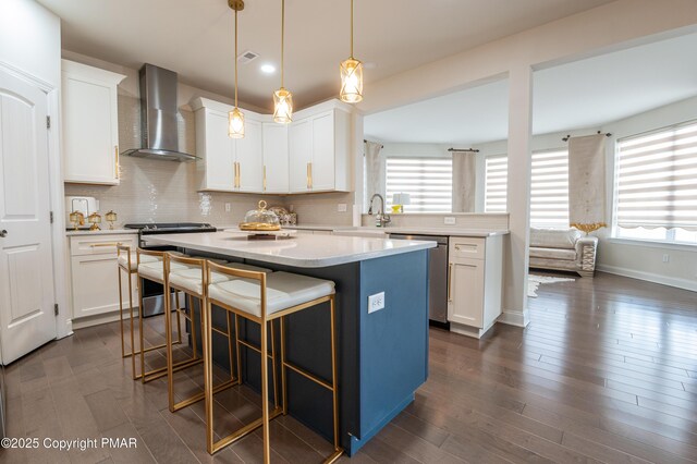 kitchen with white cabinets, a center island, wall chimney exhaust hood, light countertops, and appliances with stainless steel finishes