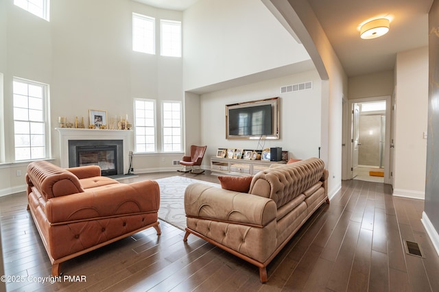 living room featuring dark wood-type flooring, visible vents, arched walkways, and a fireplace with flush hearth