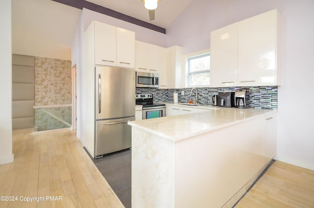 kitchen with appliances with stainless steel finishes, light wood-style flooring, backsplash, and a peninsula