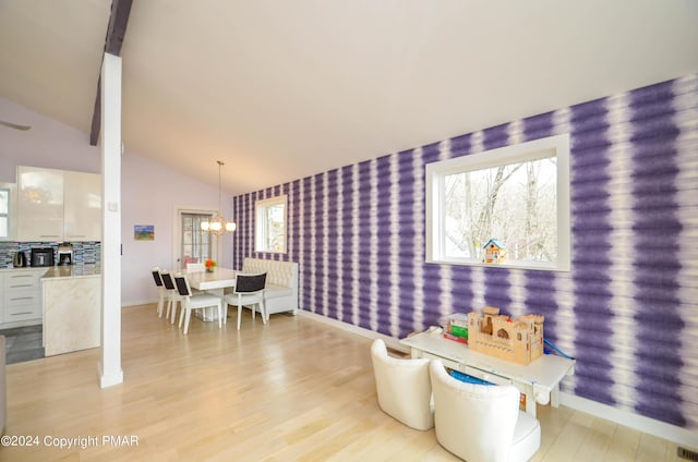 dining room featuring wallpapered walls, light wood finished floors, baseboards, lofted ceiling, and an inviting chandelier