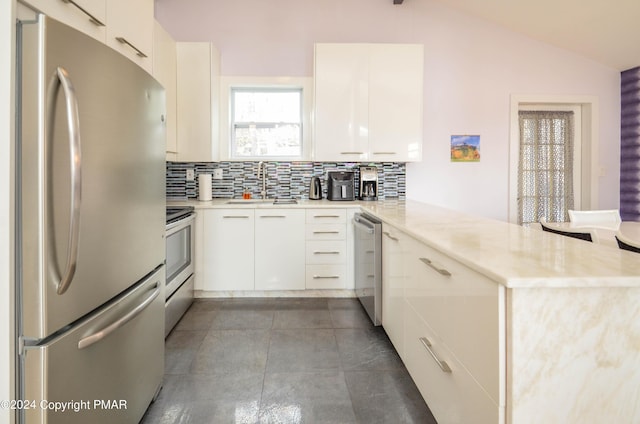 kitchen with a peninsula, a sink, vaulted ceiling, appliances with stainless steel finishes, and backsplash