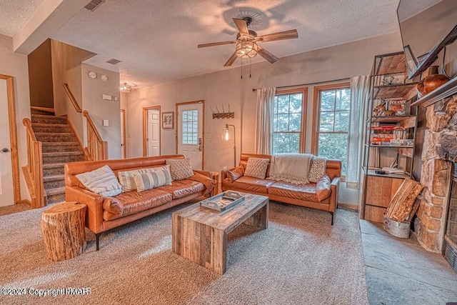 living room with a stone fireplace, stairway, a ceiling fan, and a textured ceiling