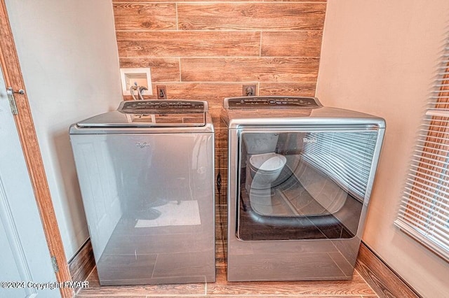 laundry room featuring wooden walls, wood finished floors, laundry area, and washing machine and clothes dryer