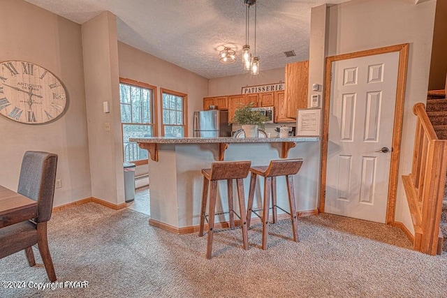 kitchen featuring light carpet, brown cabinets, a kitchen bar, and freestanding refrigerator