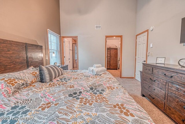 bedroom featuring visible vents, light colored carpet, a high ceiling, and connected bathroom