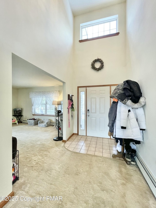 carpeted foyer entrance with a baseboard heating unit, a towering ceiling, and a healthy amount of sunlight