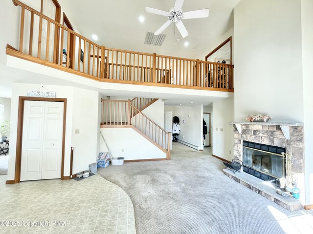 carpeted living room featuring a high ceiling, a stone fireplace, and ceiling fan