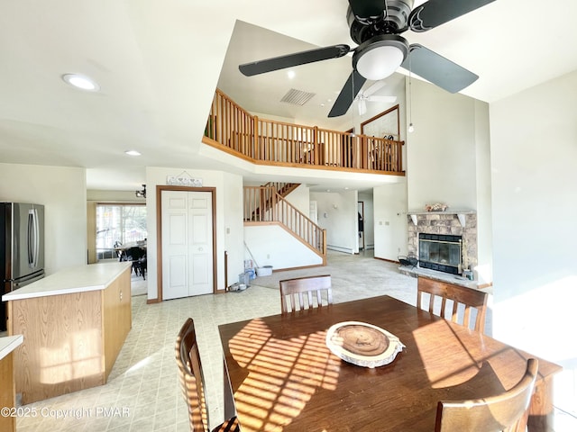 dining area featuring a stone fireplace, ceiling fan, and a towering ceiling