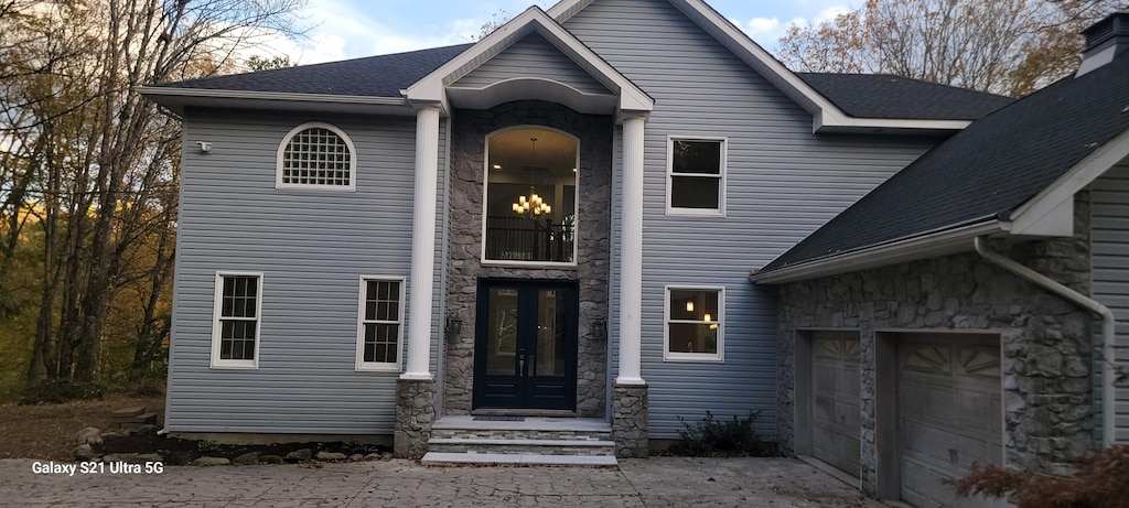 view of front of property with stone siding, french doors, and roof with shingles