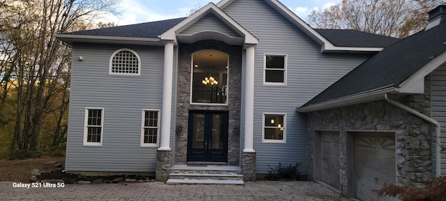 view of front of property with stone siding, french doors, and roof with shingles