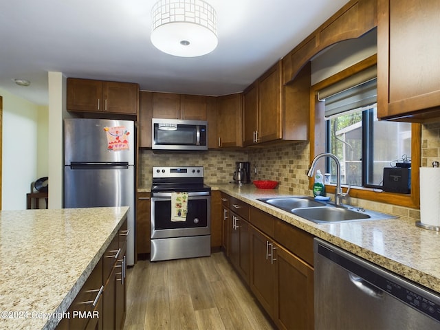 kitchen with light wood finished floors, decorative backsplash, appliances with stainless steel finishes, light countertops, and a sink