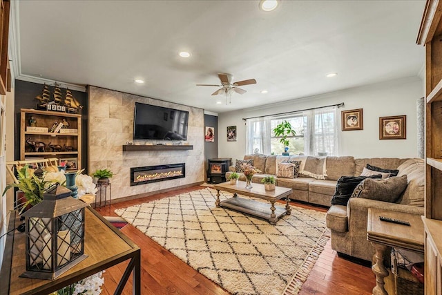 living area featuring ornamental molding, wood finished floors, recessed lighting, a large fireplace, and ceiling fan