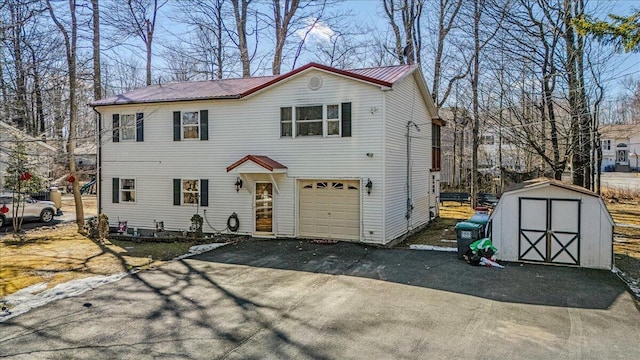 view of front of house with aphalt driveway, metal roof, a storage shed, an outbuilding, and an attached garage