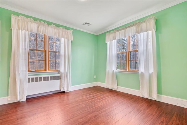 spare room featuring a wealth of natural light, visible vents, radiator heating unit, ornamental molding, and wood finished floors