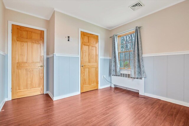 unfurnished room with crown molding, visible vents, radiator heating unit, wood finished floors, and wainscoting