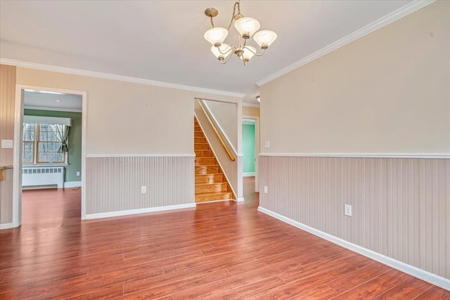 spare room featuring stairway, a chandelier, a wainscoted wall, radiator heating unit, and wood finished floors