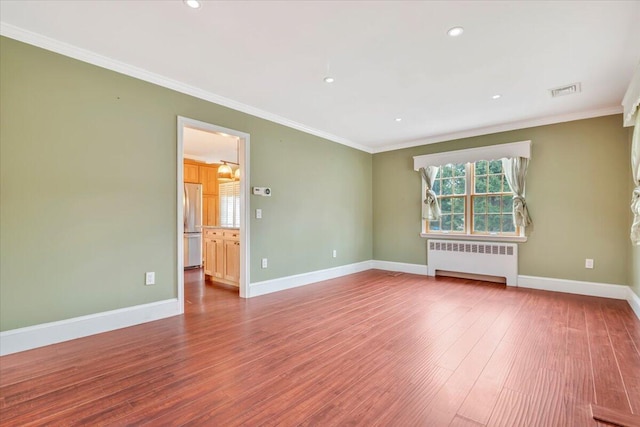 empty room featuring radiator, ornamental molding, wood-type flooring, baseboards, and visible vents