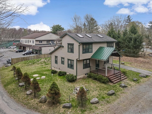 view of side of home with fence, roof with shingles, covered porch, and a yard
