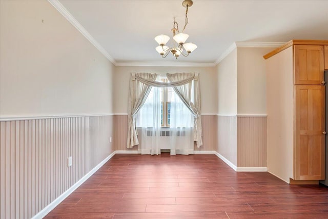 unfurnished dining area with dark wood-style flooring, ornamental molding, a notable chandelier, and wainscoting