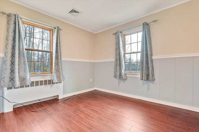 unfurnished room with visible vents, radiator heating unit, wood finished floors, and wainscoting