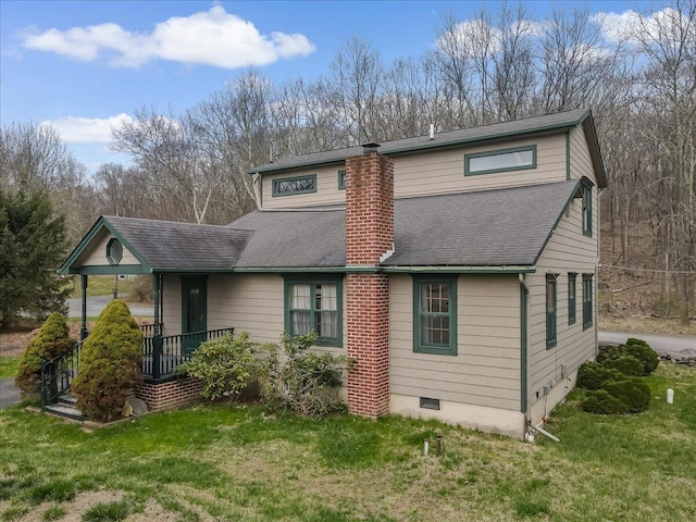 back of property with a chimney, a porch, a shingled roof, and a lawn