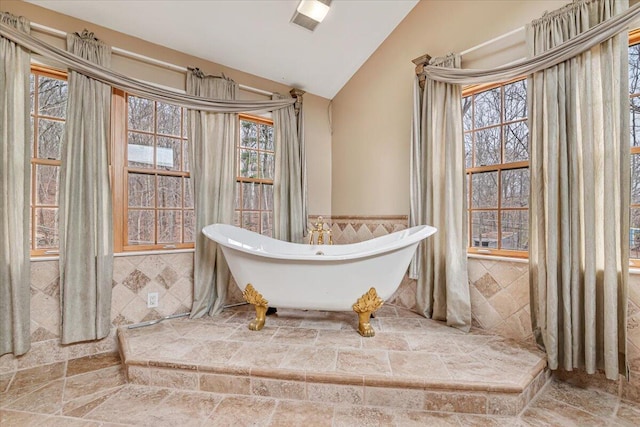 full bathroom with a freestanding tub, a wainscoted wall, vaulted ceiling, and tile walls