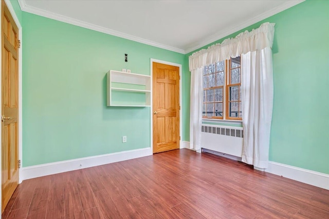 unfurnished room with wood finished floors, baseboards, crown molding, and radiator