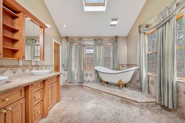 bathroom featuring stone tile flooring, vanity, visible vents, a freestanding bath, and lofted ceiling