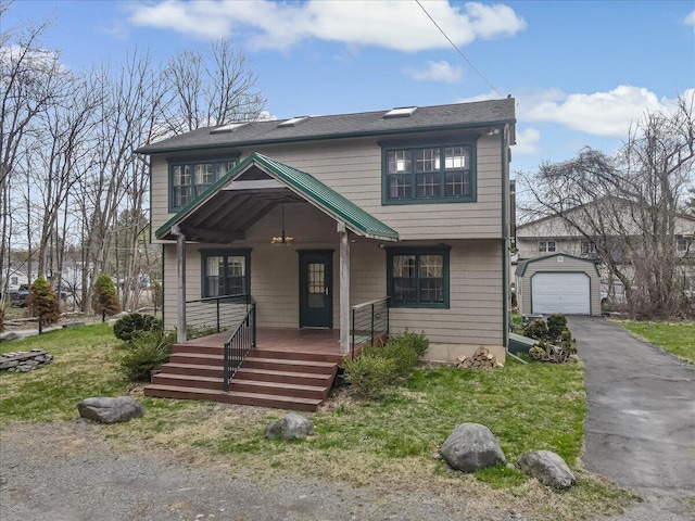 view of front facade with a porch, a front yard, a garage, an outbuilding, and aphalt driveway