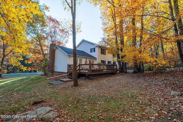 rear view of property featuring a wooden deck, a chimney, and a yard