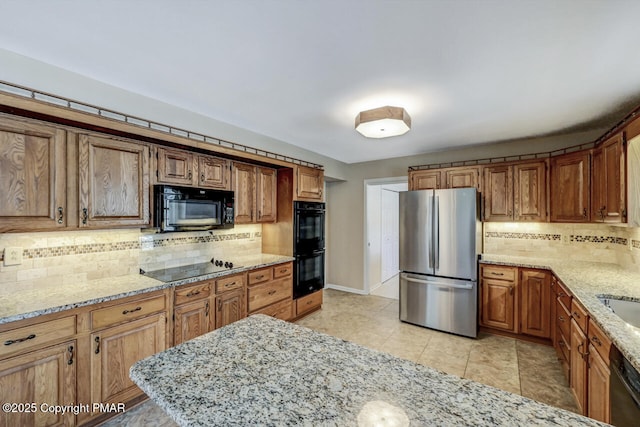 kitchen featuring brown cabinetry, backsplash, black appliances, and light stone countertops