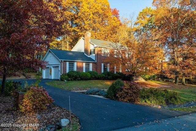 colonial inspired home featuring a garage, aphalt driveway, a front yard, a chimney, and brick siding