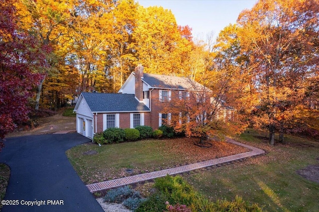 view of front of property with aphalt driveway, brick siding, a chimney, an attached garage, and a front yard