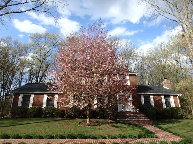 view of property hidden behind natural elements with brick siding, a chimney, and a front yard