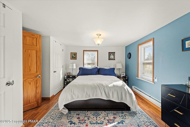 bedroom with a baseboard radiator, wood finished floors, and baseboards