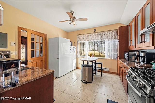 kitchen featuring stainless steel gas range, white fridge, ceiling fan, dark stone counters, and a baseboard heating unit