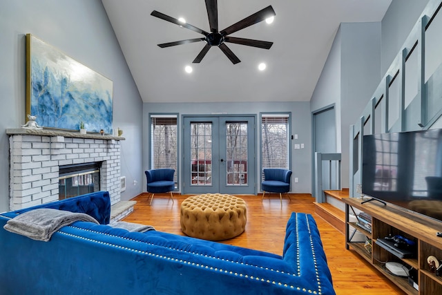 living area featuring french doors, a fireplace, wood finished floors, and a ceiling fan