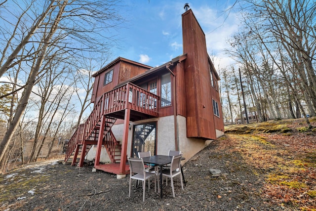 back of property with a chimney, a wooden deck, and stairs