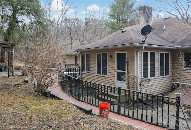 view of front of house featuring a deck, a chimney, and roof with shingles