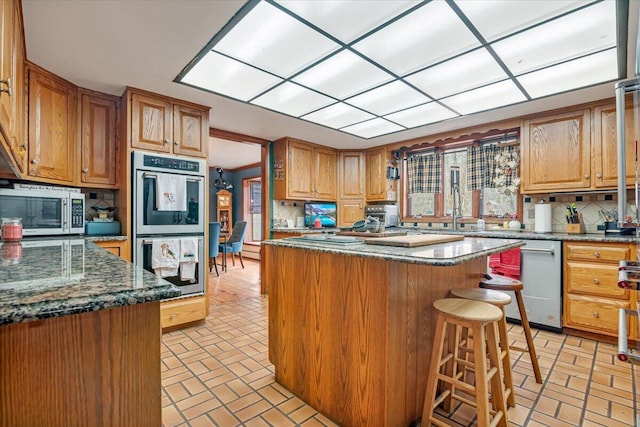 kitchen with a kitchen breakfast bar, backsplash, a center island, stainless steel appliances, and brick floor