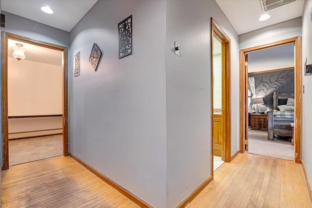 hall with baseboards, light wood-style floors, visible vents, and a baseboard radiator