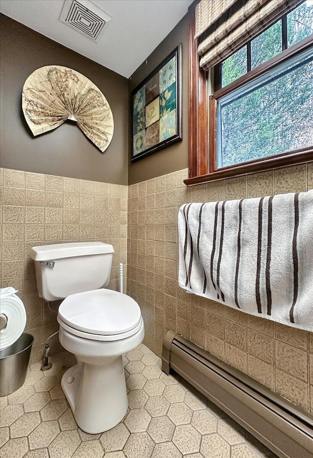 half bath with baseboard heating, toilet, tile walls, and visible vents