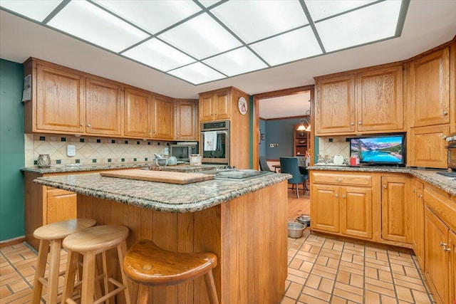 kitchen with light stone counters, tasteful backsplash, a center island, appliances with stainless steel finishes, and a breakfast bar area