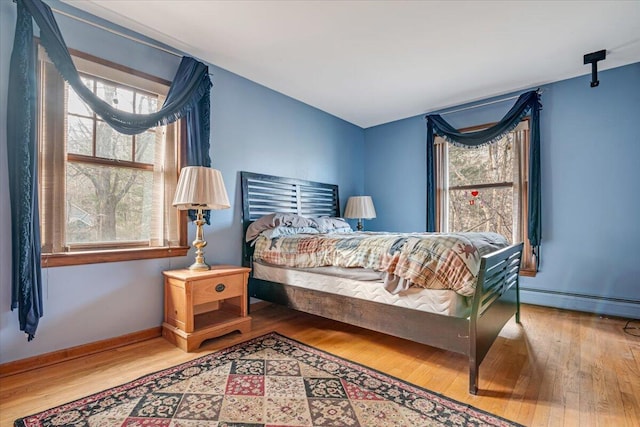 bedroom featuring a baseboard radiator, baseboards, and wood finished floors