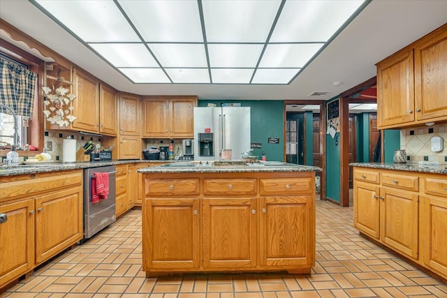 kitchen featuring a center island, light stone counters, decorative backsplash, appliances with stainless steel finishes, and brown cabinetry