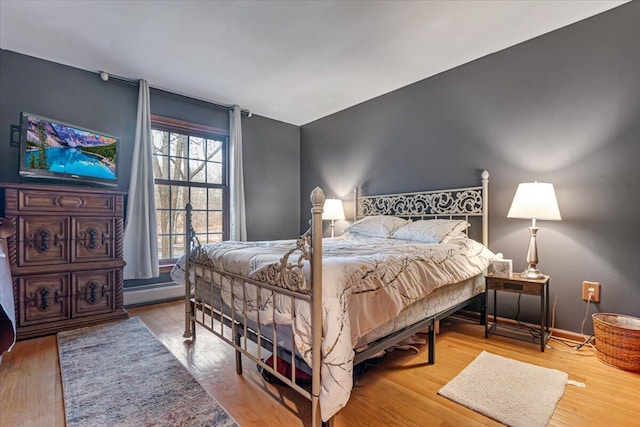 bedroom featuring a baseboard radiator, baseboards, and wood finished floors